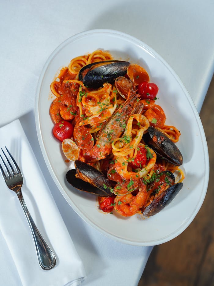 A vibrant seafood pasta dish with shrimp, mussels, and cherry tomatoes, garnished with herbs.