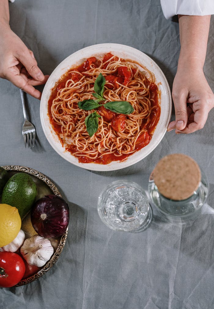 Top view of a plate of spaghetti with tomato sauce, surrounded by fresh ingredients on a table.