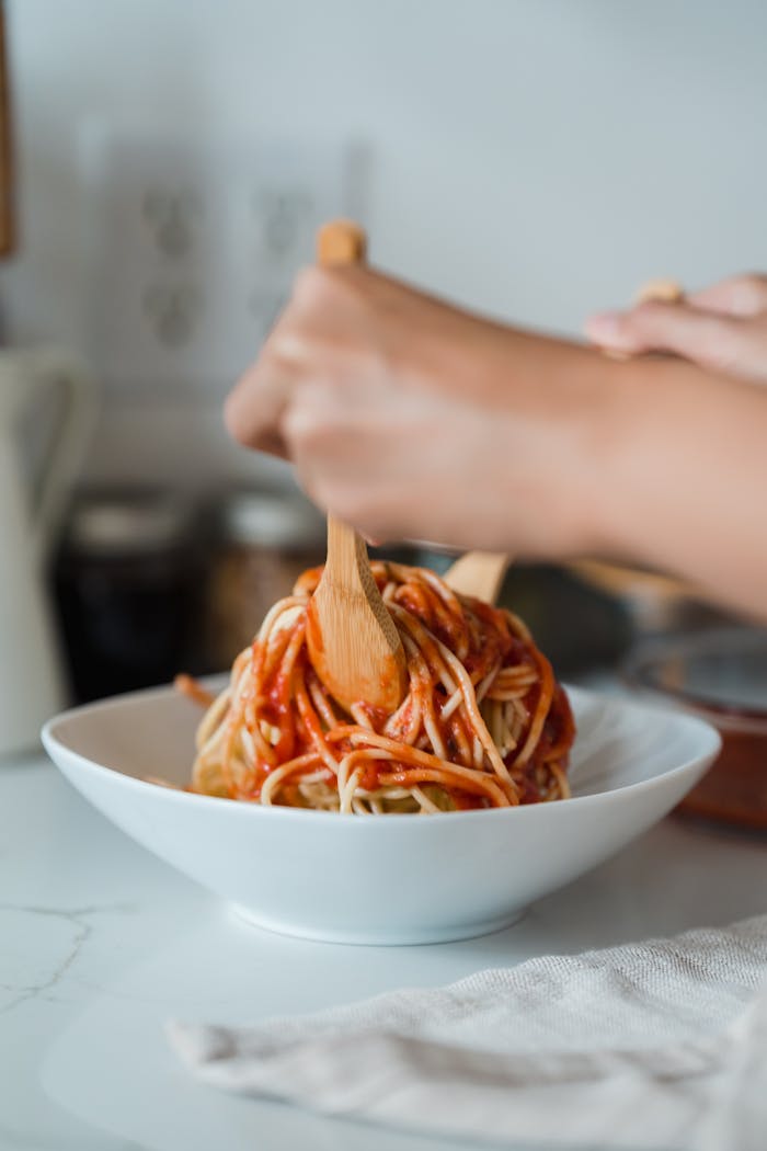 A close-up of hands mixing delicious spaghetti with utensils in a modern kitchen setting.